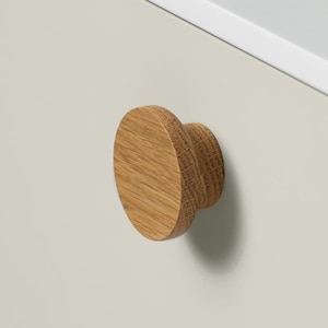 May include: A circular wooden cabinet knob with a natural wood grain. The knob is fixed to a pale grey cabinet door. The cabinet has a white top edge.
