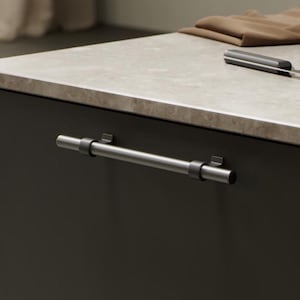 May include: A close-up of a modern kitchen cabinet with a dark grey door and a brushed nickel bar handle. The handle is mounted horizontally with two small brackets. The countertop is light grey with a marble-like pattern.