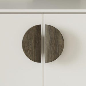 May include: A white cabinet featuring two semi-circular cabinet pulls with a wood-grain finish. The pulls are a dark brown colour and are attached to the white cabinet doors. The cabinet is part of a larger piece of furniture.