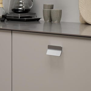 May include: A kitchen setting with coffee-making equipment. A glass carafe and a pour-over coffee maker are on a countertop. Two light-coloured cabinet doors with silver handles are in the foreground. A wooden chopping board and small ceramic cups are also visible.