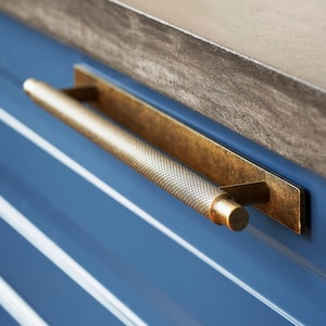 May include: A gold-toned cabinet pull with a textured, diamond-shaped pattern. The pull is mounted on a blue cabinet door.