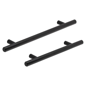 May include: Two black, cylindrical cabinet pulls with a T-shaped design. The pulls are made of a matte black material and are set against a white background. The pulls are different sizes, suggesting they are for different sized drawers or cabinets.