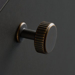 May include: A black metal knob with a brass finish and a ridged design. The knob is attached to a black surface.