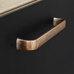May include: A brushed copper cabinet pull with a curved design. The pull is mounted on a black cabinet door.