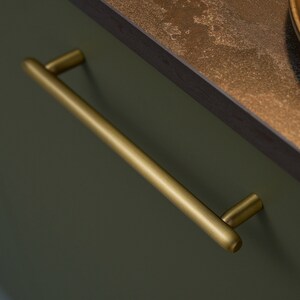 May include: A brushed gold cabinet pull with rounded edges.