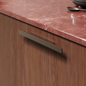 May include: A close-up of a kitchen cabinet with a rectangular, brushed metal handle. The cabinet is made of wood with a reddish-brown finish. A red marble countertop is visible in the background.