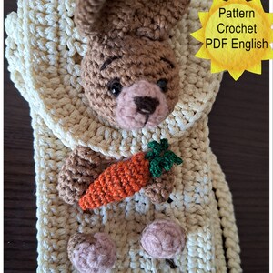 Könnte beinhalten: Ein gehäkeltes Amigurumi-Häschen, das eine Karotte hält. Das Häschen ist braun mit einer rosa Nase und schwarzen Augen. Das Häschen sitzt in einer gehäkelten cremefarbenen Tasche mit einem Riemen. Die Tasche hat ein Muster aus kleinen Löchern. Das Bild enthält den Text "Pattern Crochet PDF English".