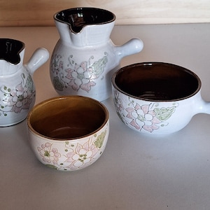 Peut inclure: Ensemble de quatre pièces de cuisine en céramique avec des motifs floraux. L'ensemble comprend un petit pichet, un petit pot à crème, un petit bol et un grand bol avec une poignée.