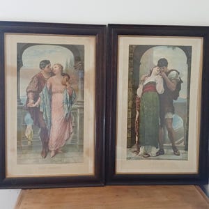 May include: Two framed prints depicting romantic scenes. The prints feature couples in classical attire, set against architectural backgrounds. The frames are dark brown, and the artwork has a vintage aesthetic, with soft colors and detailed figures.