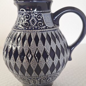 Peut inclure: Un pichet en céramique bleu avec un motif en losanges et des motifs floraux complexes. Le pichet a une anse et une petite inscription qui indique "0.5".