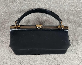 Bolso de mano vintage de cuero de 1963, negro, con marco dorado y asa superior.