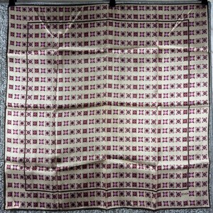 May include: A cream-colored square scarf with a repeating pattern of small, dark pink and purple floral-like shapes. The scarf has a dark brown border and is made of a silky material. The scarf is likely vintage.