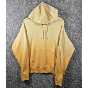 May include: A Champion brand hoodie in a gradient yellow colour scheme. The hoodie features a drawstring hood, a kangaroo pocket, and ribbed cuffs and hem. A small Champion logo is visible on the chest.