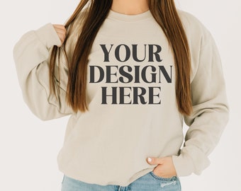 May include: A beige sweatshirt with long sleeves and a crew neck. The text "YOUR DESIGN HERE" is printed in black on the front of the sweatshirt.
