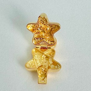 May include: A gold-toned star-shaped locket with a hinged opening. The locket is decorated with intricate details and a raised design. The locket is open, revealing a detailed interior.