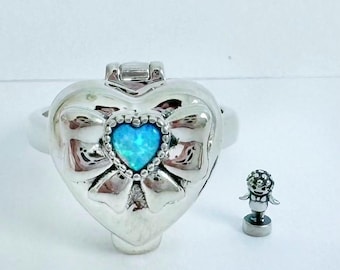 May include: A silver heart-shaped ring with a blue opal heart and a bow design. The ring is open and has a small silver charm attached to it.