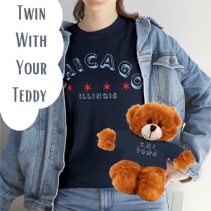 Puede incluir: Una camiseta azul marino con el texto "CHICAGO ILLINOIS" en una fuente retro. La camiseta se combina con un oso de peluche marrón que lleva una camiseta azul marino con el texto "CHI TOWN" en una fuente retro.