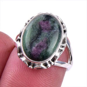 Op de afbeelding: Zilveren ring met een ovale edelsteen. De edelsteen is groen met paarse en zwarte insluitsels. De zetting van de ring heeft een decoratieve, geschulpte rand.