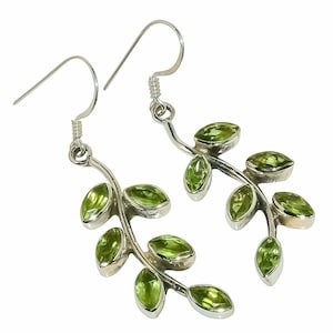 Puede incluir: Un par de pendientes colgantes de plata con un diseño de rama y múltiples piedras preciosas de peridoto verde claro en talla marquesa. Cada pendiente cuelga de un gancho de plata curvado y muestra una serie de hojas adornadas con piedras facetadas.