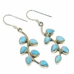 Puede incluir: Un par de pendientes colgantes de plata con un diseño de rama curva adornado con varias piedras pequeñas de color azul claro en forma de lágrima. Cada pendiente cuelga de un sencillo gancho de plata, mostrando un acabado de metal pulido y piedras lisas de color azul cielo estilo cabujón dispuestas en un patrón simétrico y orgánico.