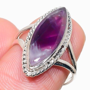 May include: A marquise-cut purple and white amethyst gemstone set in a polished silver ring. The stone is surrounded by a twisted rope-style metal border, and the band features a split-shank design that tapers towards the back of the ring.