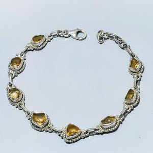 May include: A silver bracelet featuring a series of irregularly shaped, amber-colored gemstones. The stones are set in ornate, rope-textured bezels and linked by a delicate chain. The bracelet has a lobster clasp closure.