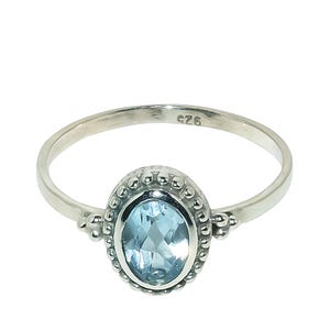 May include: A silver ring with a light blue oval gemstone set in a beaded bezel. The ring is marked "G26" on the inside.