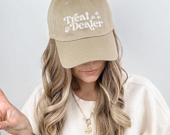 May include: A tan baseball cap with a white embroidered design that says "Treat Dealer" with paw prints.
