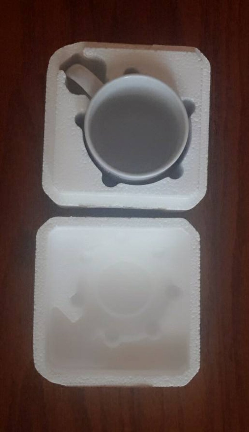 May include: A white ceramic mug with a handle, sitting in a white styrofoam packaging.