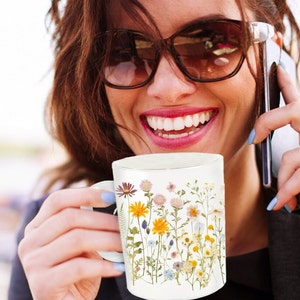 May include: White ceramic mug with a floral design featuring pressed flowers in shades of yellow, pink, blue, and purple. The flowers are arranged vertically on the mug.