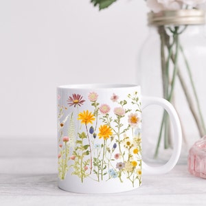 May include: White ceramic mug with a floral design featuring a variety of pressed flowers in shades of pink, yellow, and blue.
