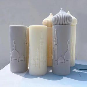Può includere: Una collezione di candele a colonna in varie tonalità di grigio e crema. Ogni candela presenta un design dettagliato di una moschea scolpito sulla superficie. Le candele hanno una forma cilindrica con la parte superiore a cupola.