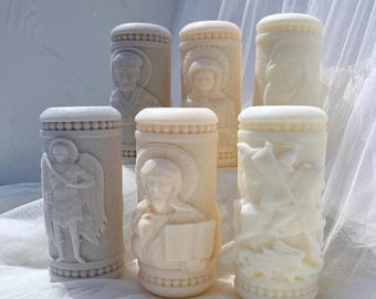 May include: A collection of six off-white, cylindrical religious figurines. Each figurine features detailed relief carvings of religious figures, including angels and saints. The carvings are set against a textured background, and the figurines have a smooth, rounded top.