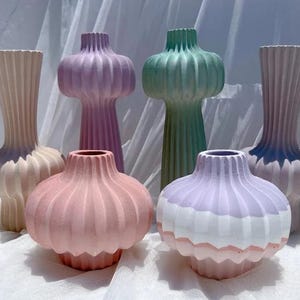 Puede incluir: Colección de seis jarrones decorativos en varios colores pastel. Los jarrones tienen un diseño acanalado y formas bulbosas, con colores como rosa, lavanda, verde y crema. Los jarrones varían en altura y estilo.