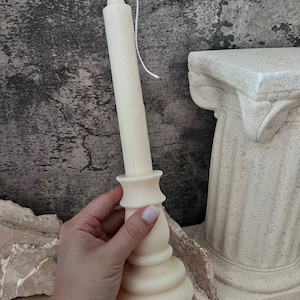 May include: Ivory candle with a classic candlestick design. The candle has a long, cylindrical body and a decorative base. A white wick extends from the top. The candle is approximately 20 cm tall.