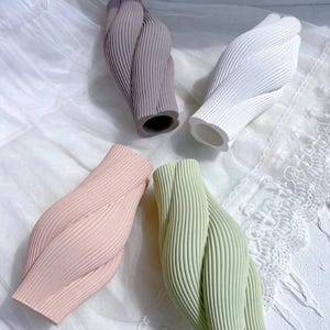 Puede incluir: Cuatro jarrones decorativos con un diseño retorcido. Los jarrones son de color gris, blanco, rosa y verde. Cada jarrón tiene una textura acanalada y una forma única, ideal para la decoración del hogar. Miden unos 20 cm de alto.
