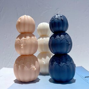Può includere: Tre pile di sfere decorative in colori pastello. Ogni pila ha tre sfere, in rosa chiaro, bianco e blu navy. Le sfere hanno una superficie strutturata con motivi floreali. Probabilmente realizzate in resina.