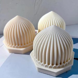 May include: Three off-white, dome-shaped objects with vertical ribbed detailing and hexagonal bases. The objects have a smooth, clean appearance and are arranged on a light blue surface. The design resembles a stylized architectural form, possibly for decorative or functional use.