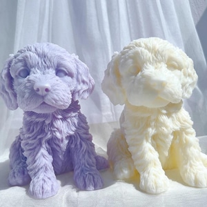 May include: Two dog-shaped sculptures. One is a soft lavender color, and the other is a creamy off-white. Both are sitting upright with detailed fur textures, and are placed on a white surface.