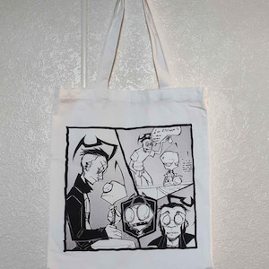 May include: A white tote bag featuring a black and white comic strip design. The comic strip depicts a character with green skin and large eyes. The text in the comic strip reads "I or ZITTIM'S".