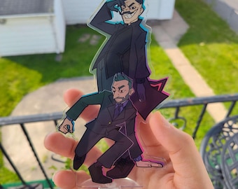 May include: A clear acrylic standee featuring two cartoon characters in suits. The top character is in a black coat, and the bottom character is in a green suit. The standee is held in a hand against a background of a house and greenery.