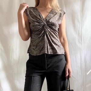 Peut inclure: Un haut à motif marron et blanc avec un col en V et un détail noué à la poitrine. Le haut est associé à un pantalon gris foncé. Un sac à main noir est tenu à la main.