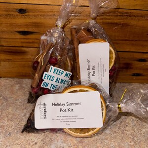 Puede incluir: Dos bolsas de plástico transparente llenas de ingredientes para un kit de olla de cocción a fuego lento para las fiestas. Las bolsas contienen palitos de canela, rodajas de naranja secas, arándanos y anís estrellado. Las bolsas están atadas con una cinta dorada y tienen una etiqueta que dice "Kit de olla de cocción a fuego lento para las fiestas".