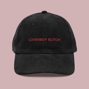 Peut inclure: Casquette de baseball en velours côtelé noir avec un texte brodé en rouge qui dit "LOVERBOY BUTCH"
