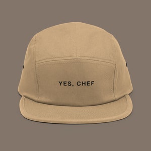 May include: A tan 5-panel baseball cap with a black embroidered logo that says "YES, CHEF".