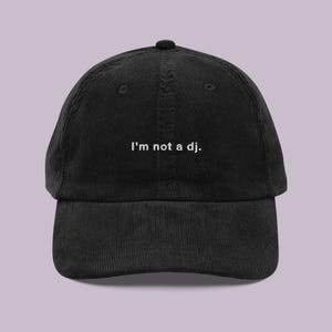 Op de afbeelding: Een zwarte corduroy baseballpet met de tekst "I'm not a dj." geborduurd in wit op de voorkant.