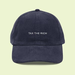 Può includere: Cappellino da baseball in velluto a coste blu navy con la scritta bianca "TAX THE RICH". Il cappellino ha una visiera curva e un bottone sulla parte superiore. Stile classico.