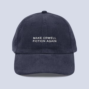 Op de afbeelding: Marineblauwe corduroy baseballcap met de witte geborduurde tekst "MAKE ORWELL FICTION AGAIN". De cap heeft een gebogen klep en een ronde kroon. Een klassieke, verstelbare hoed.