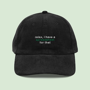 May include: Black corduroy baseball cap with the text "relax, I have a spreadsheet for that" in white and green. The cap has a curved brim and a rounded crown. A casual accessory for everyday wear.