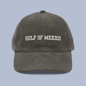 Pu&ograve; includere: Un cappello da baseball in velluto a coste verde scuro con testo ricamato bianco che recita "GULF OF MEXICO".